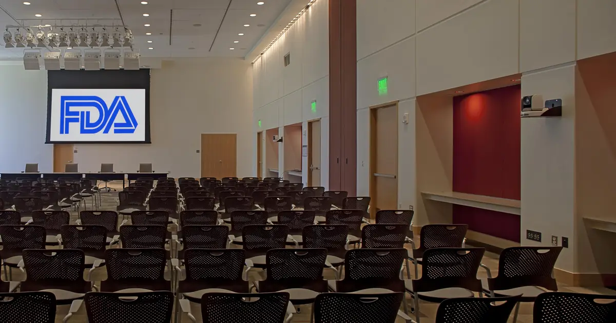 Rows of empty seats facing a screen with an FDA logo in a large public meeting room on the FDA campus.
