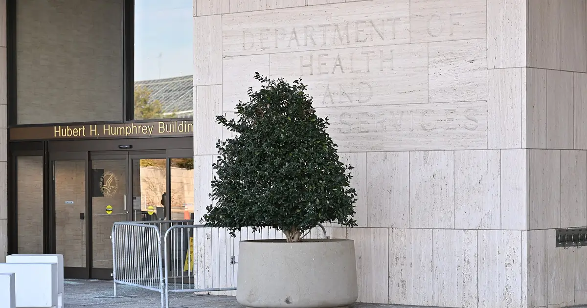 The entrance of the Hubert H. Humphrey Building in Washington, D.C., with pale stone walls carved with the department's name, glass doors and a trimmed shrub in a large planter.